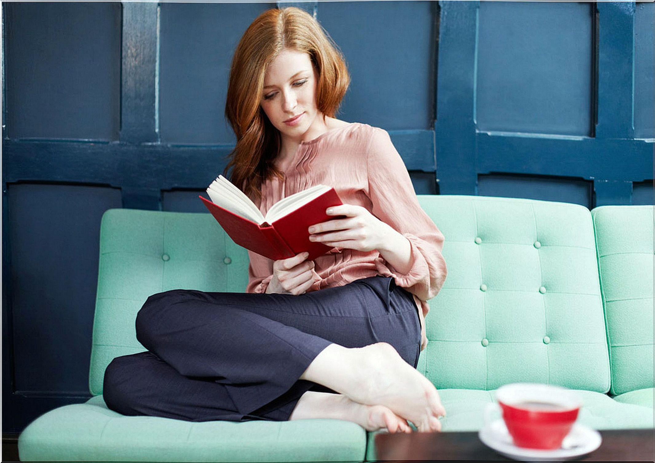 Woman reading a book sitting on a sofa.