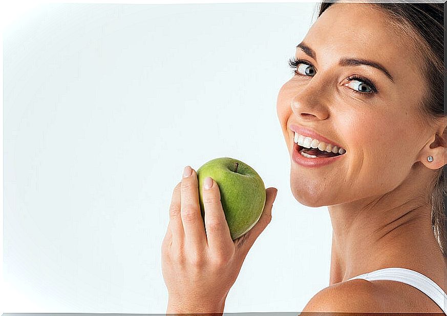 Woman smiling with a green apple in her hand.